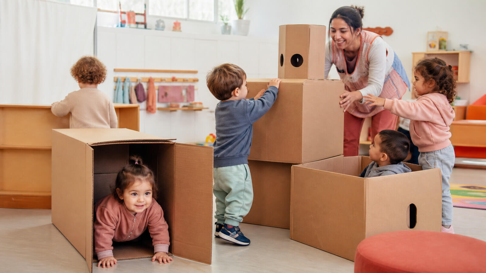 Sala de 2 jugando con cajas grandes bajo supervisión docente